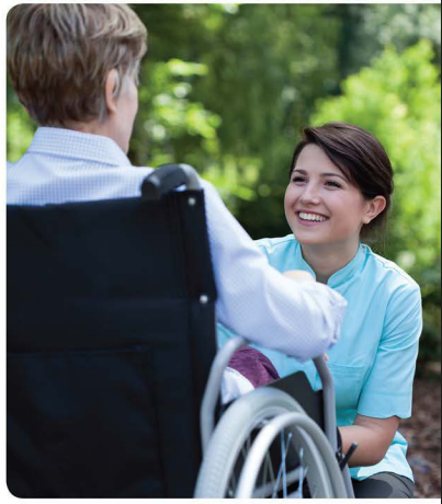 A middle-aged female caregiver kneeling and smiling at an older woman in a wheelchair